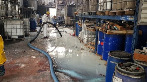 A BELFOR employee vacuums a flooded warehouse with an industrial vacuum cleaner