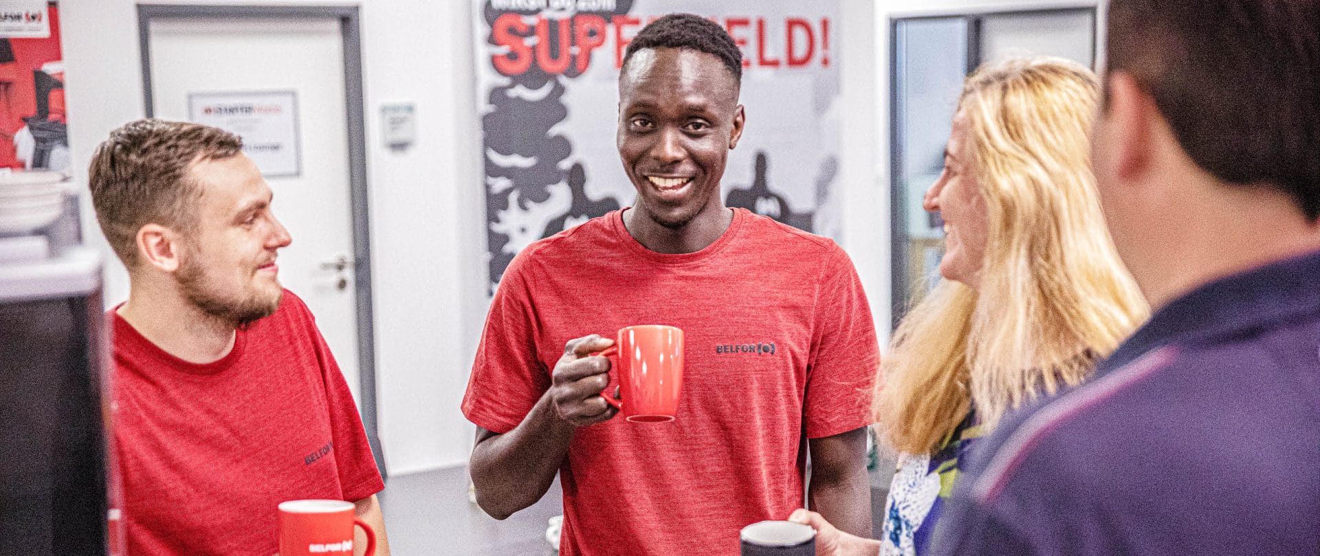 A man smiles at the camera and stands with colleagues in the kitchen